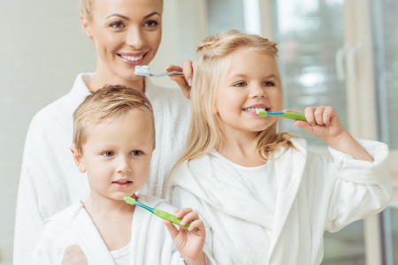 beautiful happy mother and children in bathrobes brushing teeth togetherの写真素材