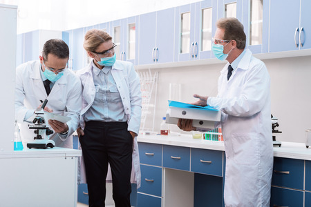 Three medical workers in sterile masks and protective glasses, discussing work in chemical...