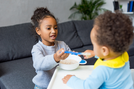 african american sister feeding her little brother at homeの写真素材