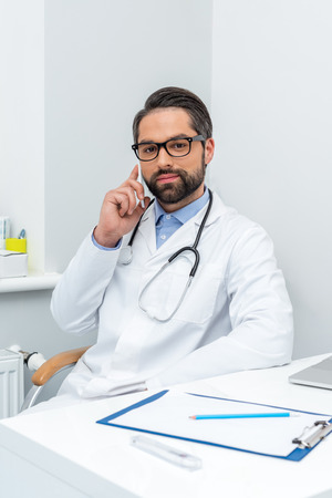 handsome young doctor talking by phone at workplaceの写真素材