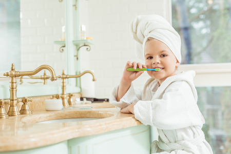 adorable little girl in bathrobe and towel brushing teeth and looking at cameraの写真素材
