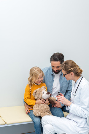 young doctor giving syrup to teddy bear of little girlの写真素材