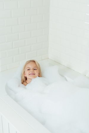 cute happy little girl sitting in bathtub with foamの写真素材