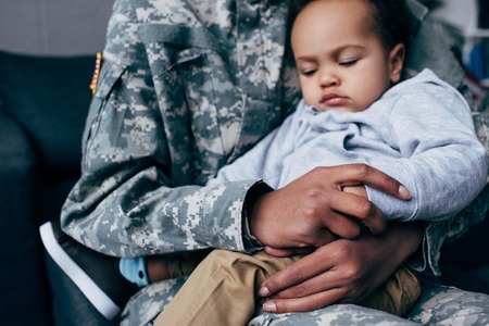 african american soldier in military uniform with her little sleeping son at homeの写真素材
