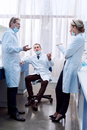 Three medical workers in lab coats and sterile masks discussing work in laboratoryの写真素材