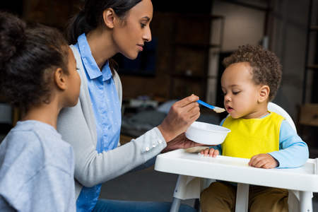 african american mother and daughter feeding little baby boy at homeの写真素材