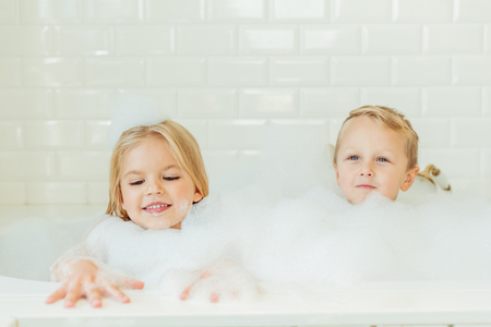 beautiful happy brother and sister playing together in bathtub with foamの写真素材