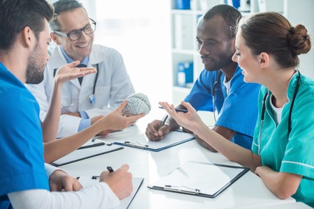 multiethnic team of doctors and general practitioner having conversation and holding plastic brain...