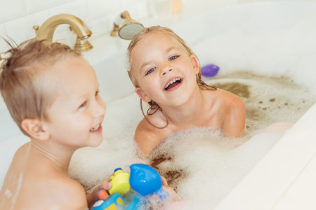 happy little brother and sister playing together in bathtubの写真素材