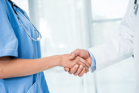 cropped shot of doctor and nurse with stethoscope shaking handsの写真素材