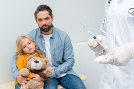 cropped shot of female doctor with syringe and blurred man with his daughter on backgroundの写真素材