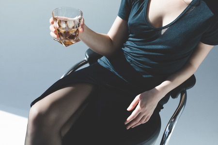cropped shot of elegant young woman holding glass of whiskey on grey 