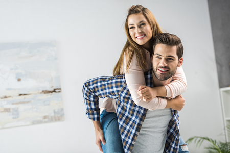 portrait of happy man piggybacking with woman at homeの写真素材
