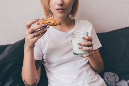 cropped shot of woman with glass of milk eating homemade toast for breakfast in bedの写真素材