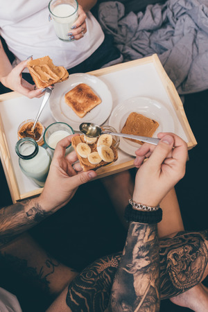 partial view of tattooed couple eating tasty homemade toasts in bed at homeの写真素材