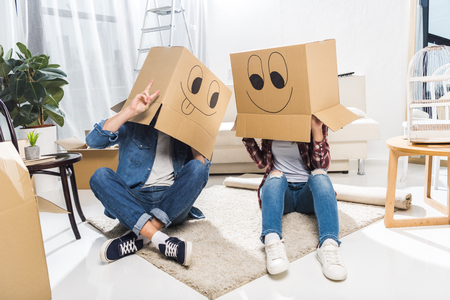 Young couple sitting on floor with boxes on their heads, that have smiley faces on themの写真素材