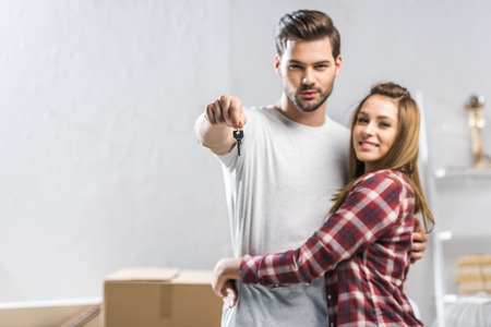 Young attractive couple hugging in living room with cardboard boxes and showing a keyの写真素材