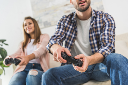 Young couple playing videogames on console while sitting on sofa in living room