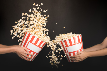 cropped shot of people spilling out popcorn from buckets isolated on blackの写真素材