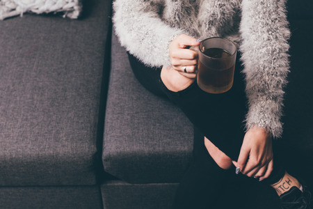 cropped shot of woman holding cup of hot tea in hand while resting on sofaの写真素材