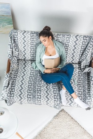 top view of brunette girl sleeping with book on couch at homeの写真素材