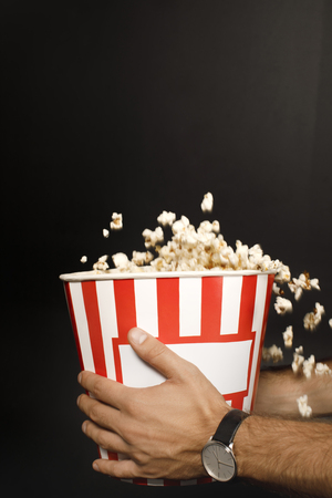 cropped shot of man holding cardboard bucket of popcorn isolated on blackの写真素材