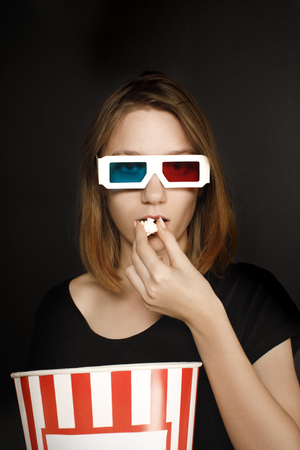 woman in 3d glasses eating popcorn and looking at camera isolated on blackの写真素材