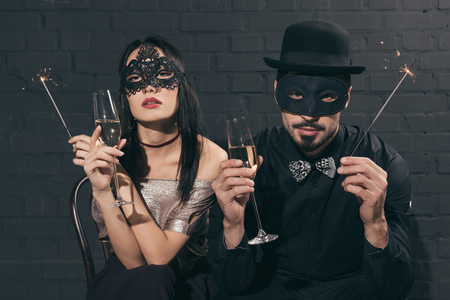 portrait of multicultural couple in christmas masks with sparkles and glasses of champagneの写真素材
