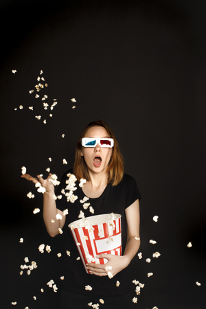 shocked woman with bucket of popcorn isolated on blackの写真素材