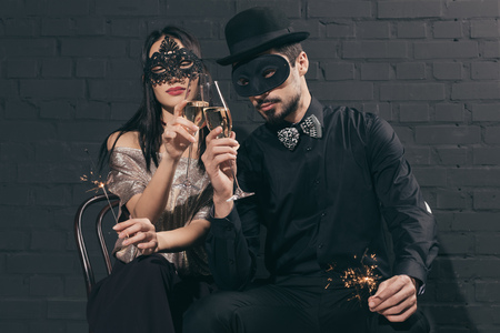 multicultural couple in christmas masks with sparkles clinking glasses of champagneの写真素材