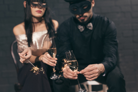 selective focus of multicultural couple in christmas masks with sparkles and glasses of champagneの写真素材