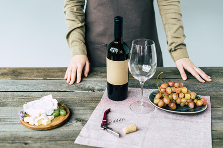 Female sommelier standing near table with wine and foodの写真素材