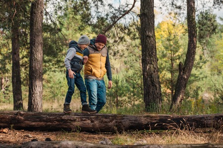 happy father and son holding hands while boy walking on log in forestの写真素材