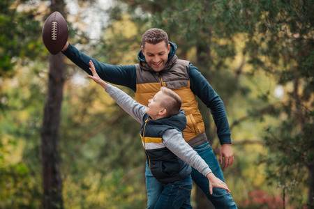 happy father and son playing with rugby ball in forestの写真素材
