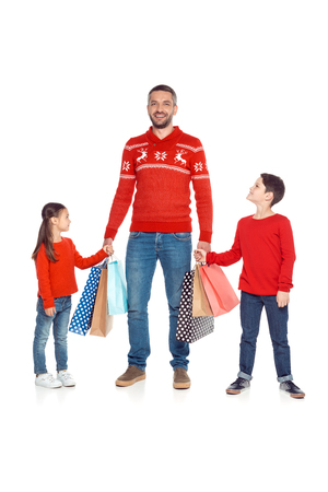 father and children in red sweaters holding hands and shopping bags, isolated on whiteの写真素材