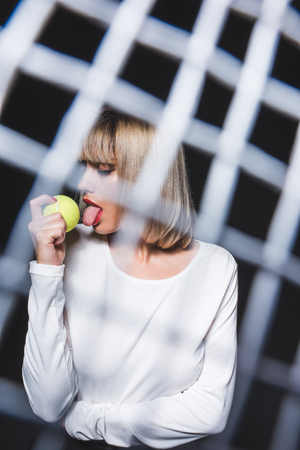 obscured view of beautiful woman licking tennis ball isolated on blackの写真素材