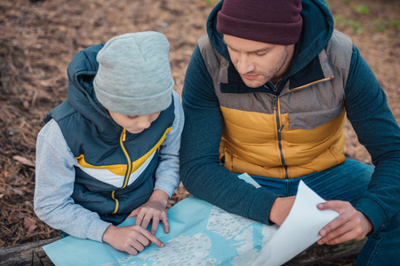 close-up view of father and son looking at map while hiking together in forestの写真素材