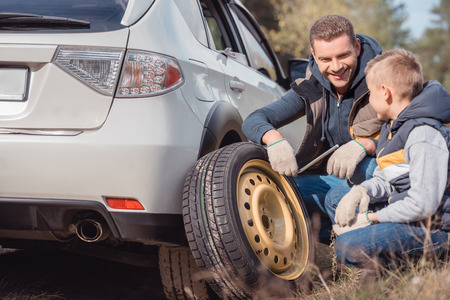 smiling father and son changing car wheel togetherの写真素材