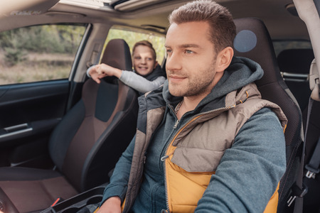 smiling little son looking at father driving car