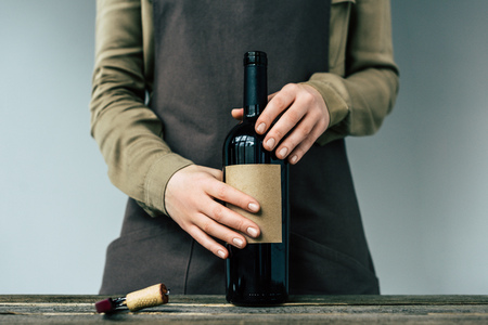 Woman in apron holding open bottle of red wineの写真素材