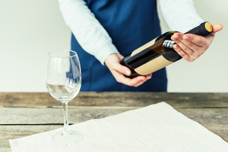 Female sommelier looking at bottle of white wine and holding it in handsの写真素材