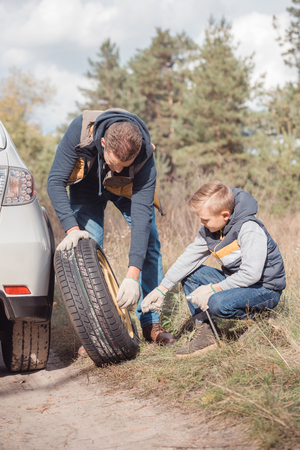 Father and son changing car wheel together in autumn forestの写真素材