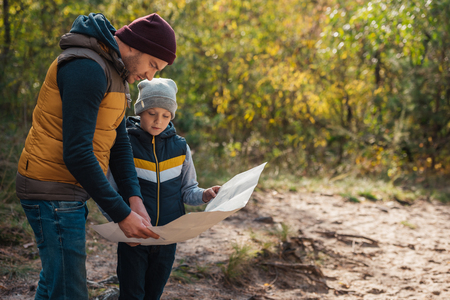 father and son holding map while hiking together in autumn forestの写真素材