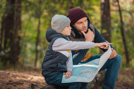 father and son holding map and pointing away with finger in forestの写真素材