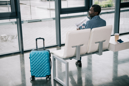 Rear view of Middle aged Businessman holding newspaper and looking away in the airportの写真素材