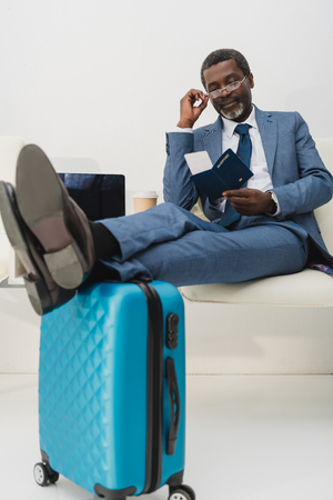 Middle aged African american businessman sitting at airport and checking departure time in the ticketの写真素材