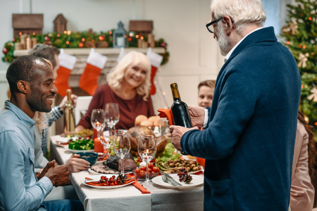 senior man with bottle of wine in front of family on christmasの写真素材