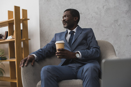African american man sitting in armchair with coffee in paper cupの写真素材