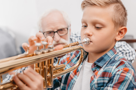 Little boy practicing playing trumpet while his grandfather is watchingの写真素材