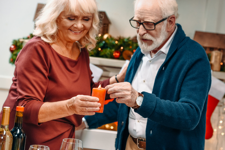 beautiful senior couple holding candle in christmas decorated roomの写真素材